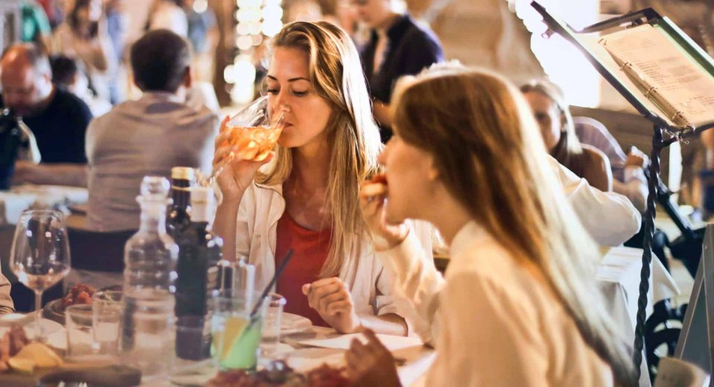 Two women are eating pizza at a restaurant.